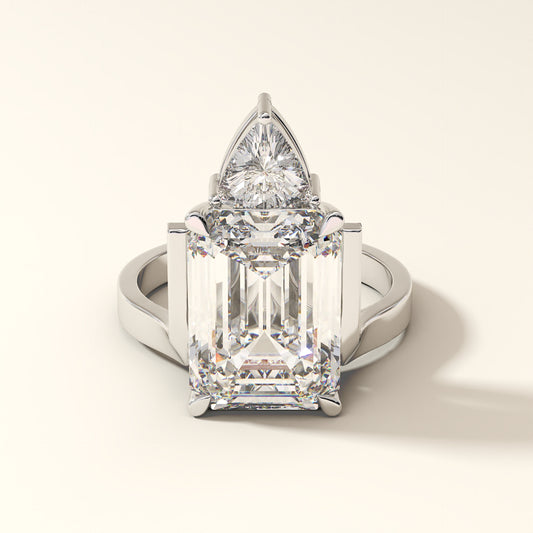 Diamond ring with emerald cut and trillion cut diamond on a light background.