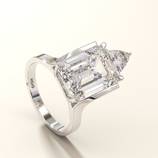 Angled view of emerald cut diamond ring with trillion-cut accent in 18K white gold.