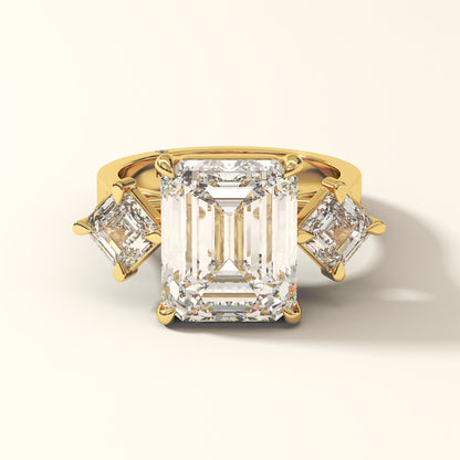 Yellow gold three stone ring with a large emerald-cut diamond and two smaller emerald-cut diamonds on a white background.