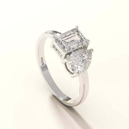 Diamond ring with two clear gemstones one emerald and one pear diamond on a white background