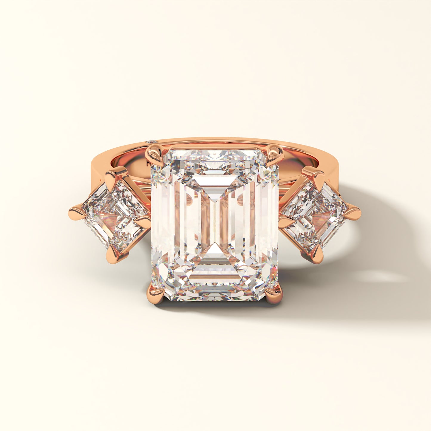 Rose gold ring with one large and two smaller emerald-cut diamonds on a white background