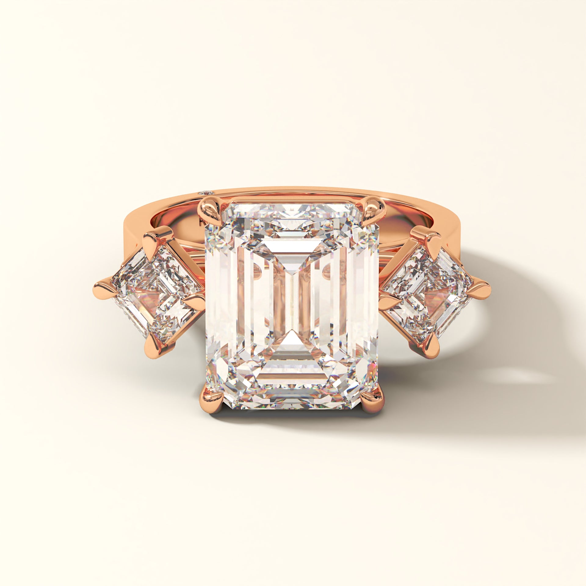 Rose gold ring with one large and two smaller emerald-cut diamonds on a white background