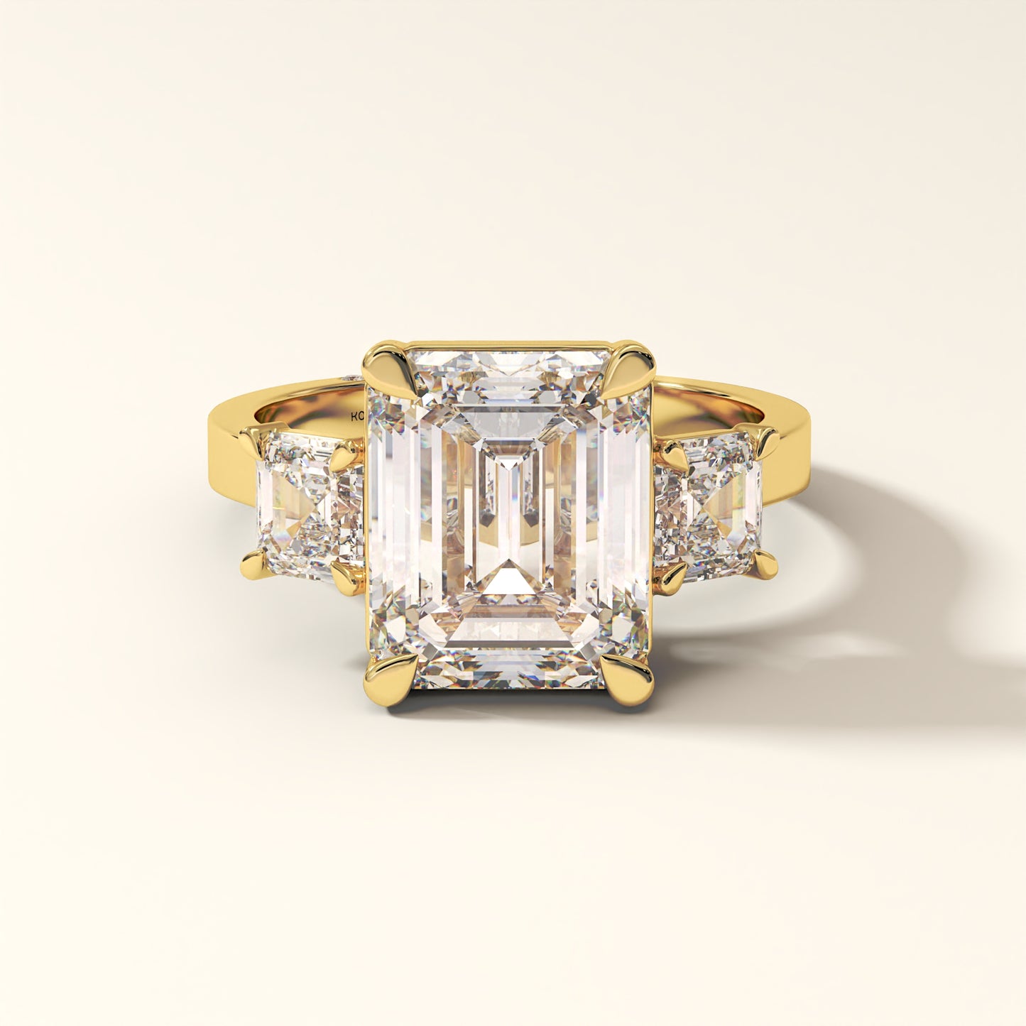 Yellow gold three-stone ring with emerald-cut and asscher-cut diamonds on a light background.