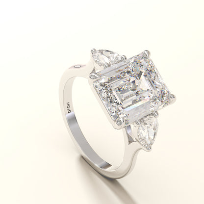 Diamond ring with emerald-cut center stone and pear side stones on a white background