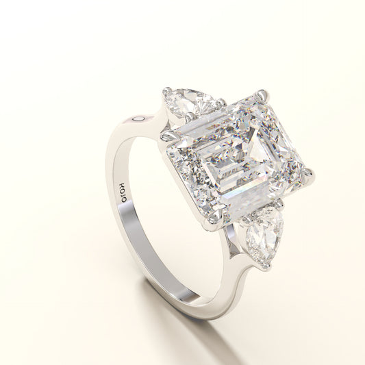 Diamond ring with emerald-cut center stone and pear side stones on a white background